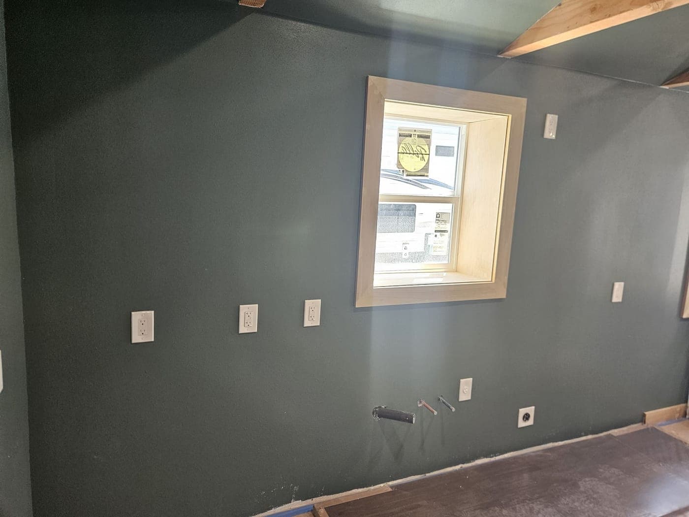 Four receptacles and a switch trimmed out on a dark green bedroom wall beside a new window casing